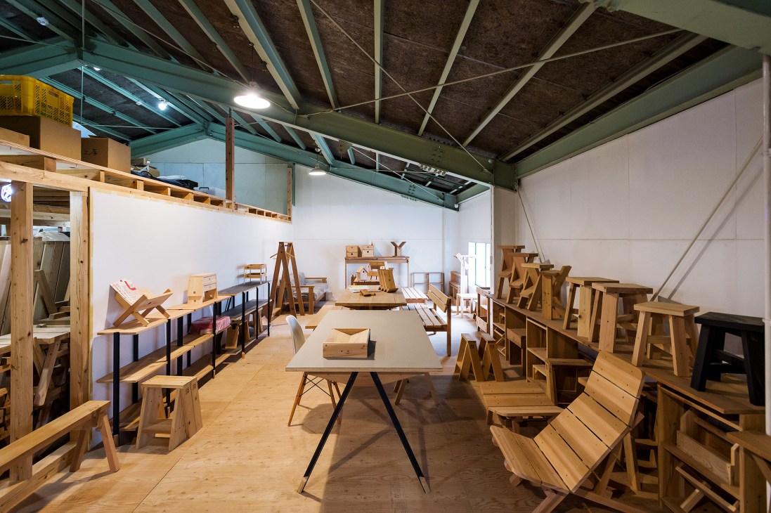 Interior of Ishinomaki Laboratory showroom displaying wooden stools, benches, and tables with industrial ceiling.