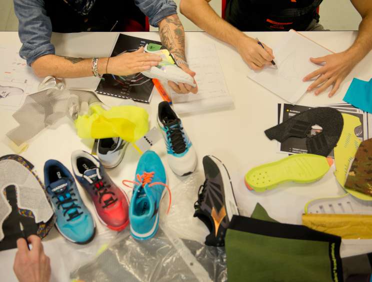 Diadora designers work at a table with colorful sports shoes, sketches, and design materials.