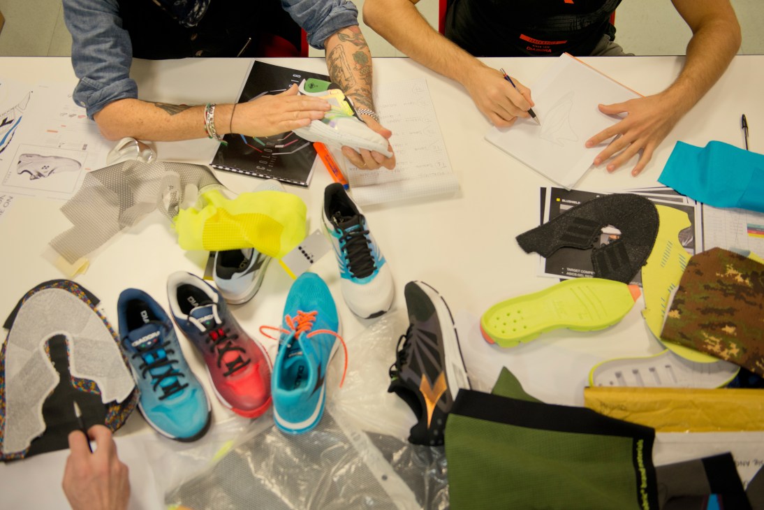 Diadora designers work at a table with colorful sports shoes, sketches, and design materials.