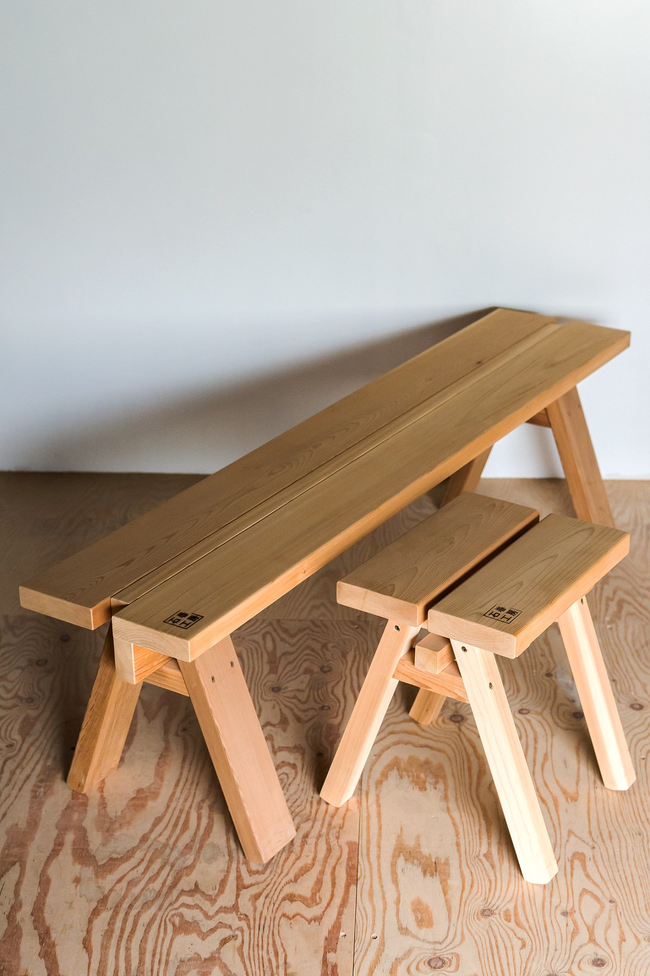 Light wood bench and two matching stools with simple A-frame legs, each branded with Japanese characters.
