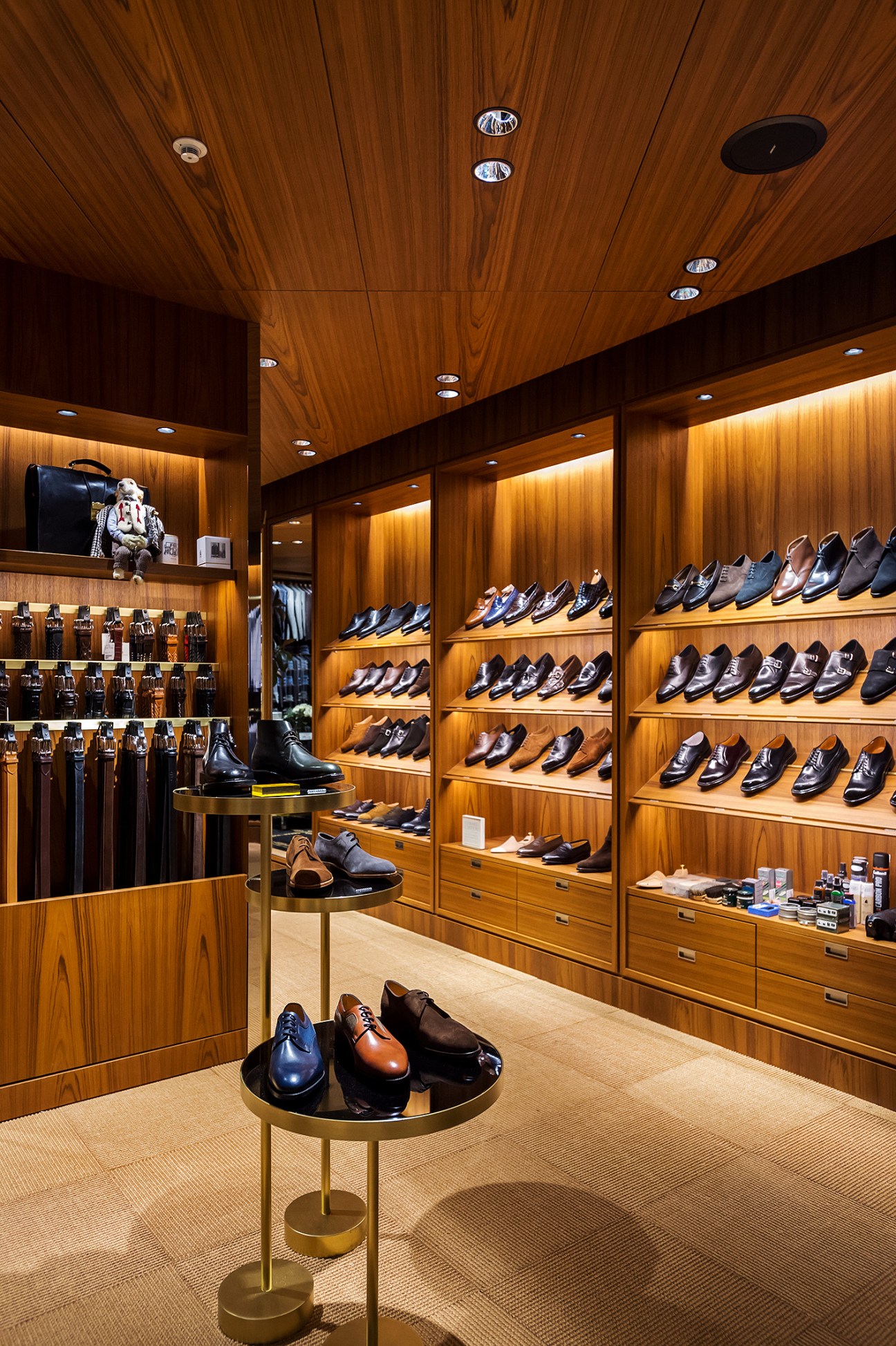Luxury menswear shoe store interior with wooden shelving displaying formal dress shoes and circular display tables