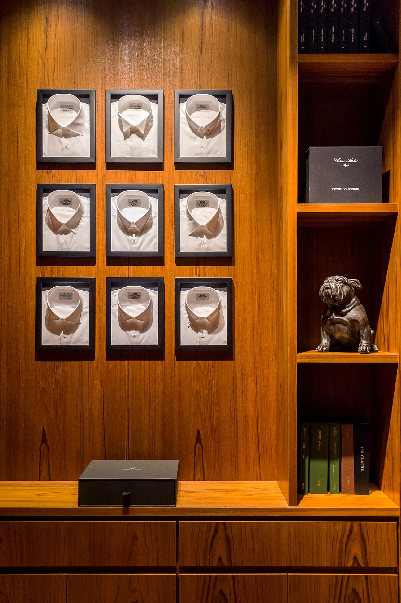 Nine white dress shirts with brown collar details displayed in black frames on wood paneling