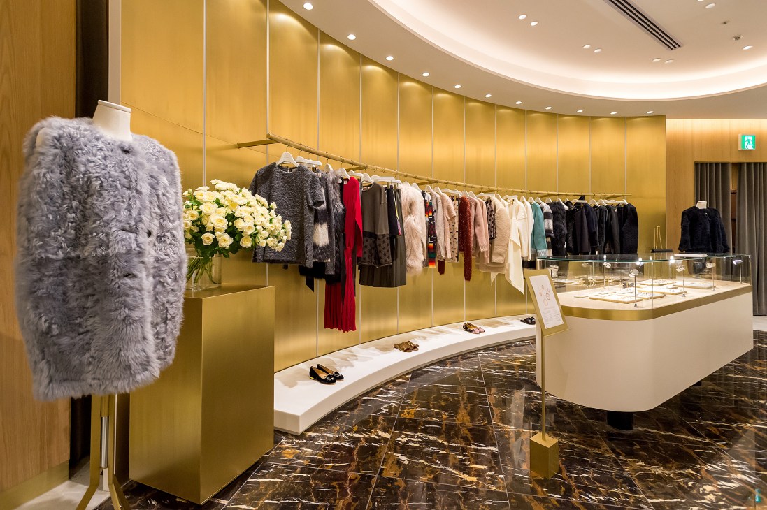 Upscale fashion boutique interior with curved gold walls, clothing racks, and marble floors