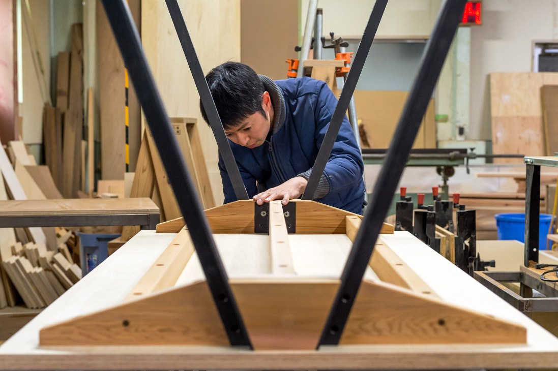 Craftsman assembling a wooden table with black metal legs in a workshop.
