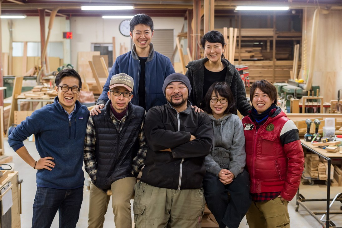 Workshop team with Takahiro Chiba standing centre in a wooden furniture workshop.