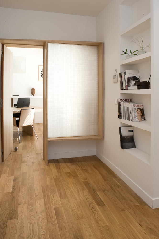 Oak-framed doorway with translucent panel opens to office workspace with pale oak parquet flooring and white shelving.