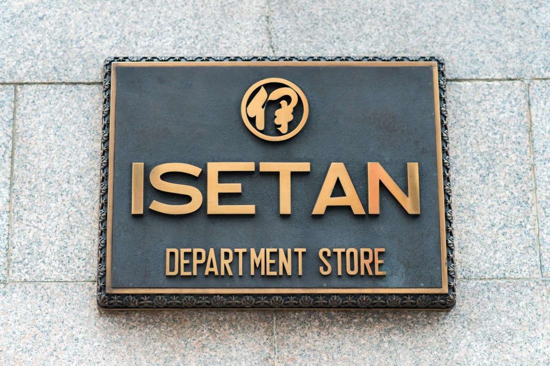 Isetan department store brass plaque with gold logo and text on dark background mounted on building facade.