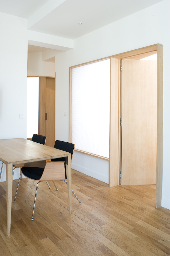 Contemporary office space with pale oak table, black chairs, and translucent oak-framed panels dividing the communal area.