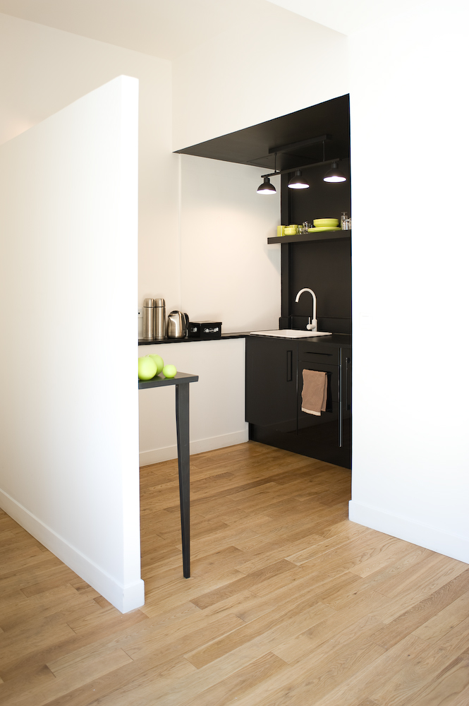 Compact kitchen corner with black-stained oak cabinetry, shelving, and pale oak parquet flooring.