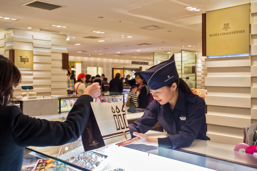 A uniformed Isetan staff member assists a customer at the department store counter.