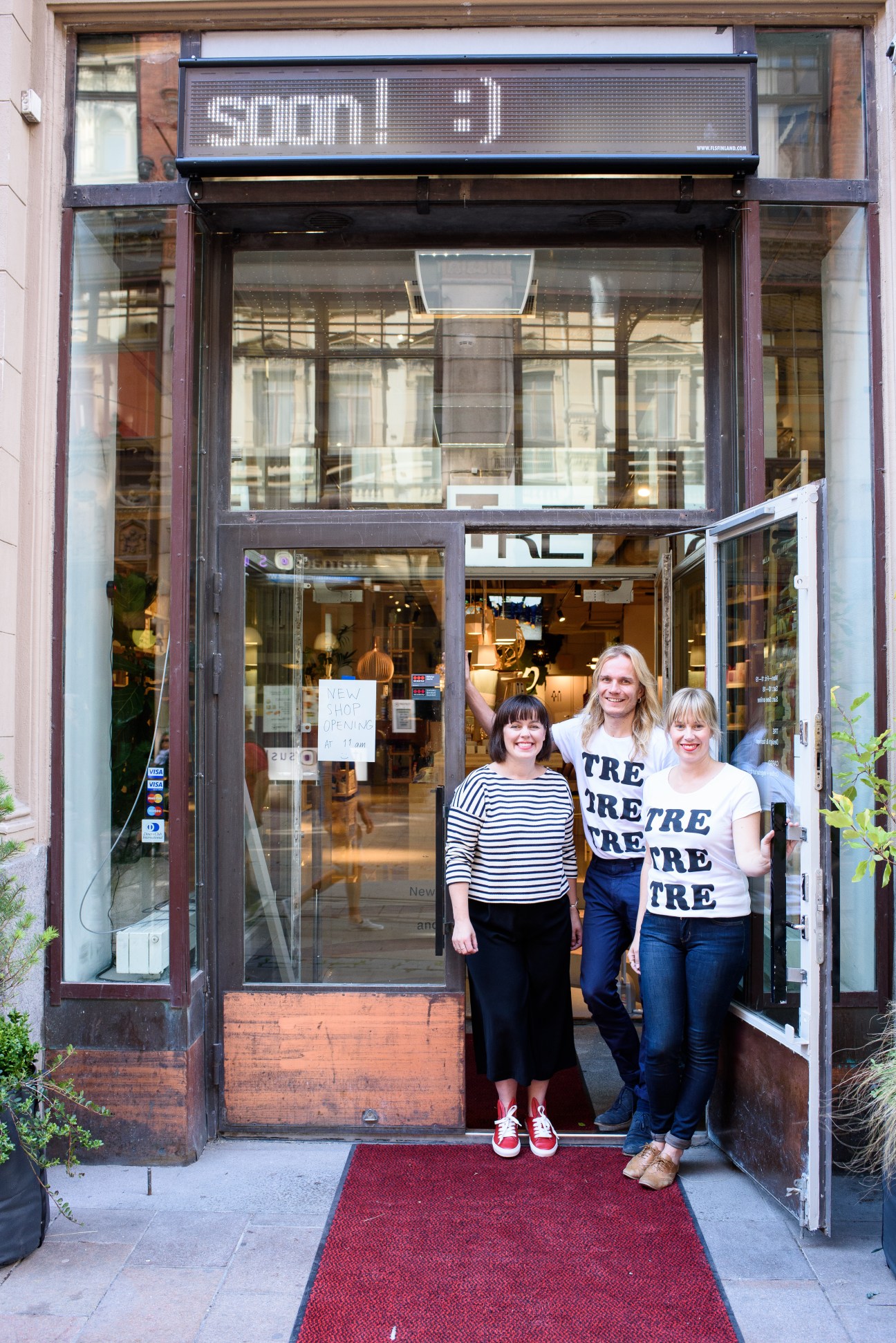 Three women stand in the doorway of TRE design shop in Helsinki, Finland, with striped and branded clothing.