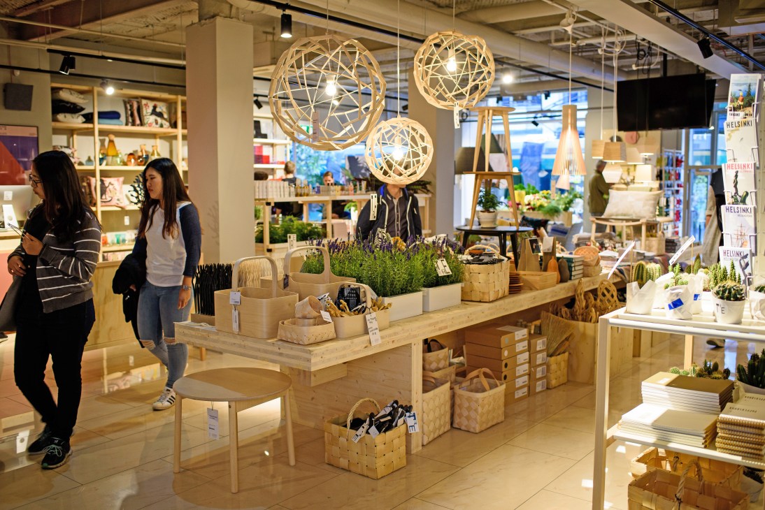 Interior of TRE design shop in Helsinki with wooden display tables, hanging woven pendant lights, and customers browsing products.
