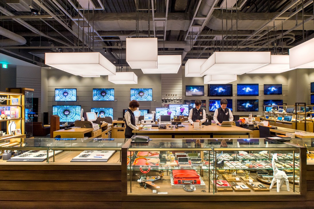 Tsutaya Electrics stationery section with staff behind counter and television department visible in background.