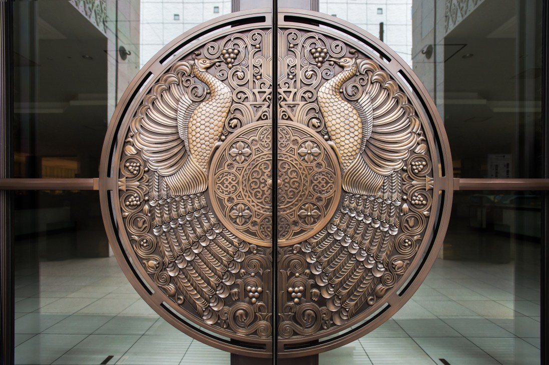 Ornate bronze circular door crest featuring two phoenixes with spread wings and decorative flourishes on Isetan's main entrance doors.