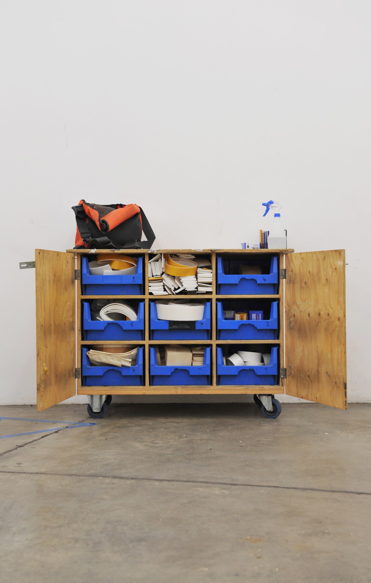 Wooden tool cabinet with blue drawers containing art handling equipment and supplies.