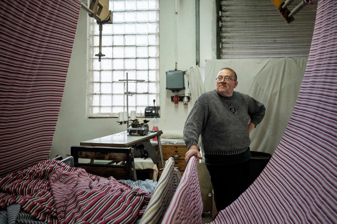 Machine operator at Sinka Es Tarsa textile factory surrounded by striped fabric rolls.