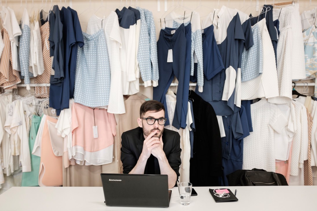István Molnár, sales and marketing manager for Use/unused, sits at a desk with a laptop in front of clothing racks.