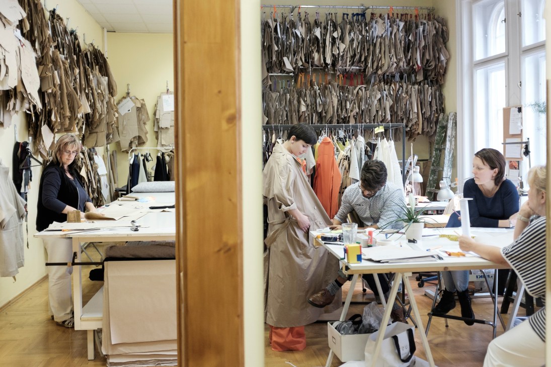 Designer and team members working at tables in a bright studio with fabric swatches covering the walls.
