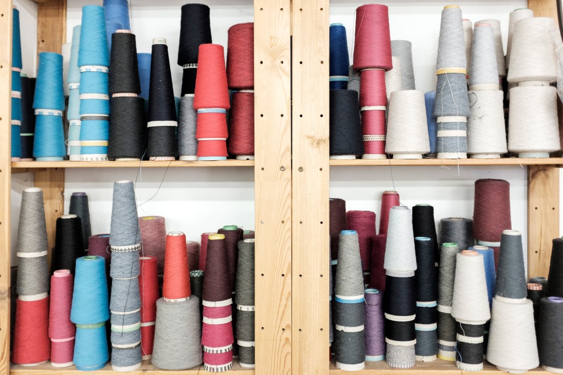 Colorful yarn spools in various shades organized on wooden shelves at Sima-Tex knitwear factory.