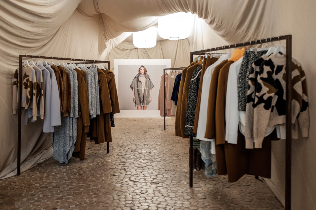 Interior of Nanushka showroom with clothing racks displaying brown, grey and patterned garments under draped ceiling.