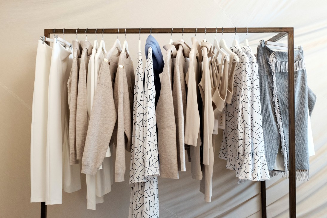 Nanushka clothing collection hanging on a wooden rail displaying neutral and patterned garments.