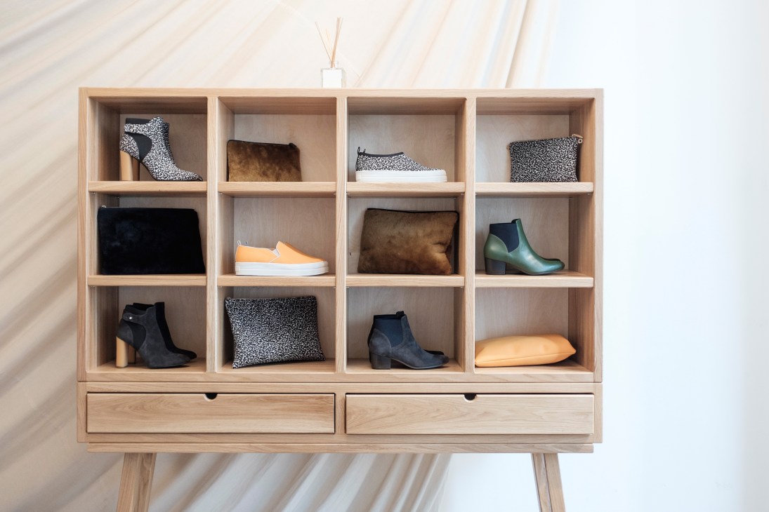 Wooden shelving unit displaying Nanushka shoes, boots, clutches and accessories with animal print and solid color patterns.