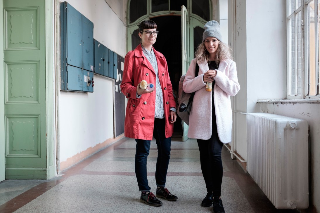 Two students stand in a corridor at Moholy-Nagy University of Art and Design wearing colorful coats.