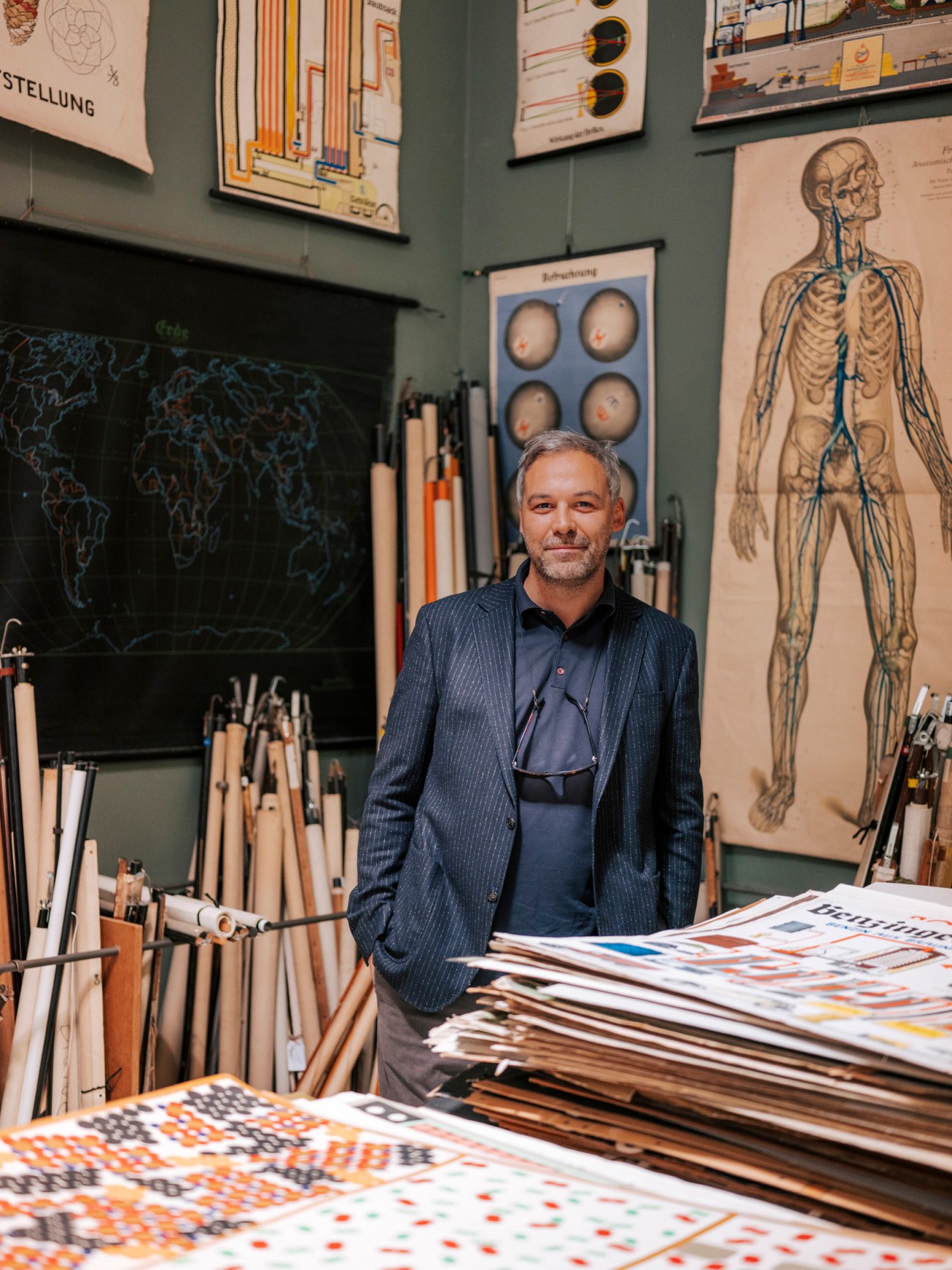 Man in pinstriped jacket stands in front of vintage charts and anatomical drawings in a graphic design shop.