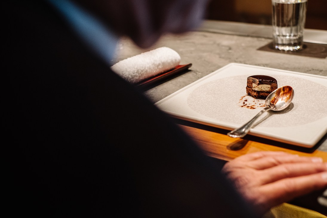 A plated chocolate mousse dessert with vanilla and macadamia on a white plate with a spoon, served at Tetsuya's restaurant.