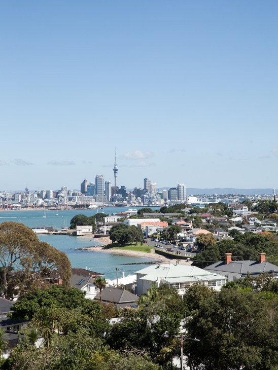 Auckland cityscape with Sky Tower visible across the harbor from Devonport's residential waterfront.
