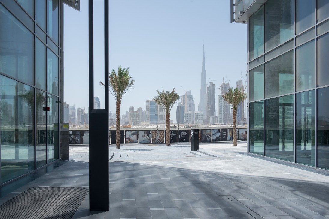 Modern glass building terrace with palm trees overlooking Dubai's skyline and Burj Khalifa.