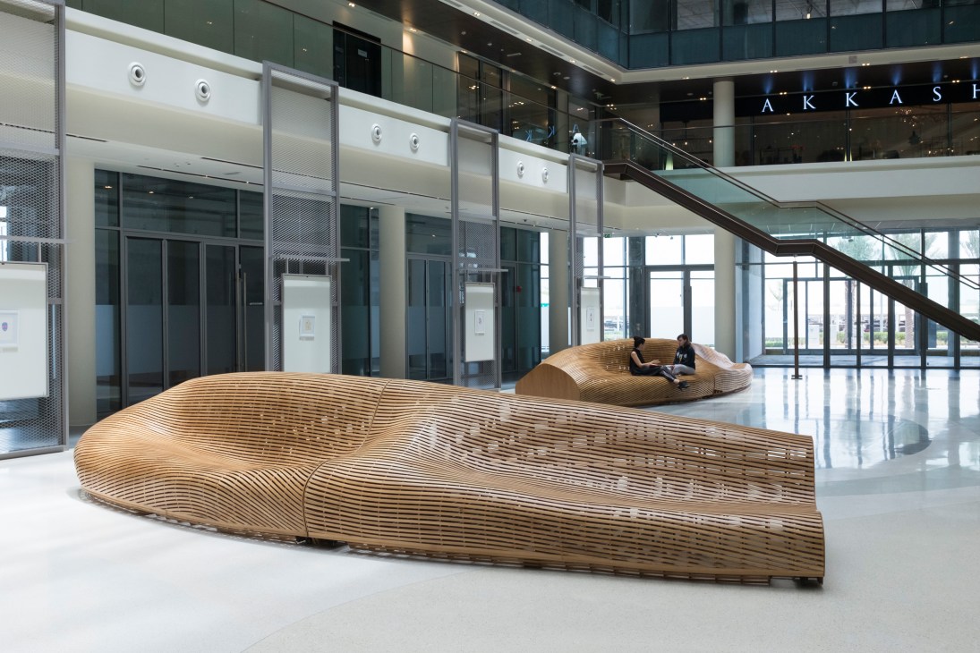 Curved wooden seating installation in a modern D3 atrium with glass elevators and staircases.