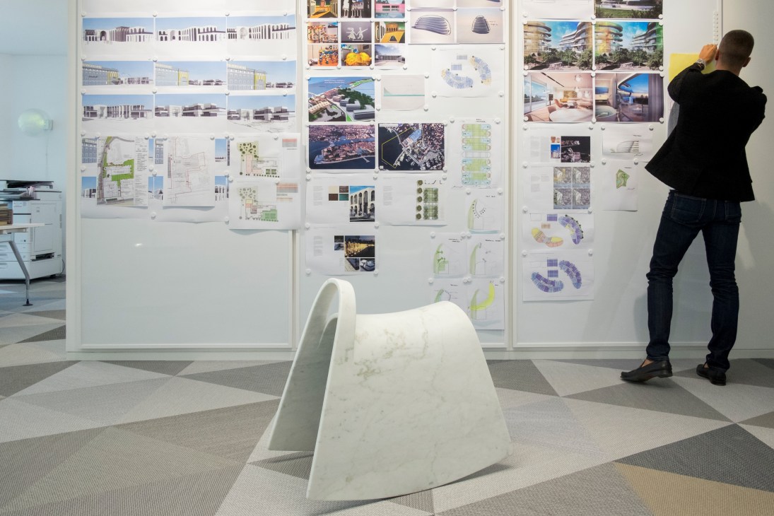 Person viewing architectural drawings and renderings pinned to white studio walls.