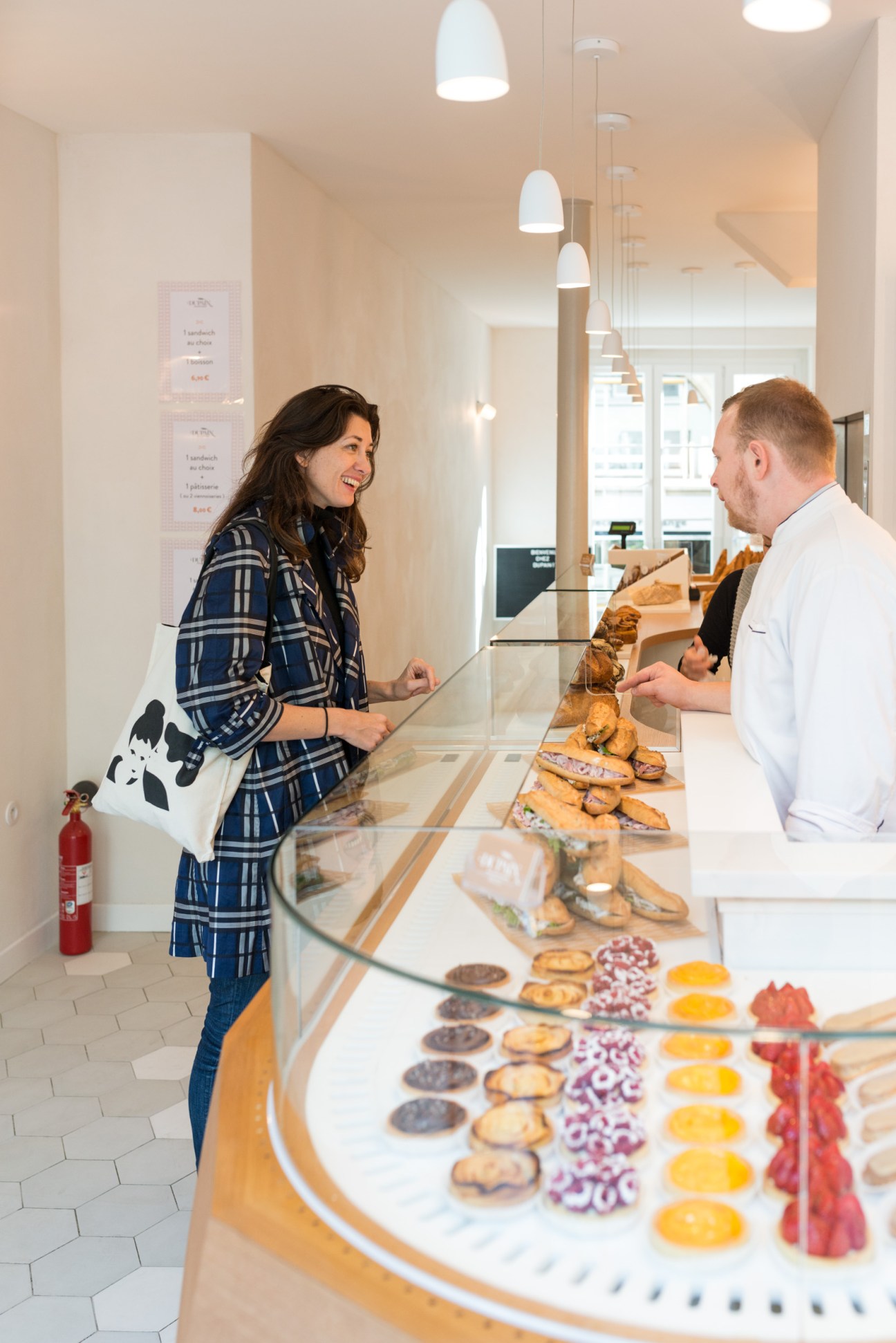 Customer and staff member at DuPain bakery counter displaying pastries and bread in Paris.