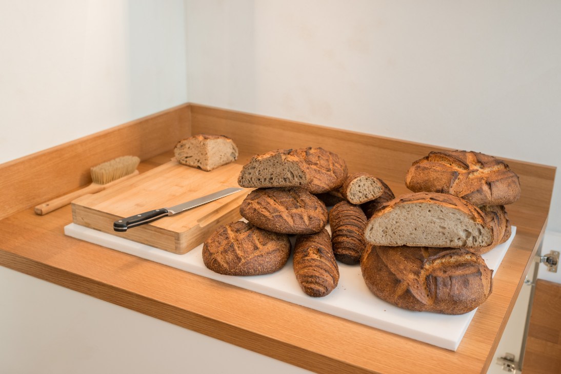 Assorted freshly baked breads and croissants displayed on a wooden tray with cutting board and knife.