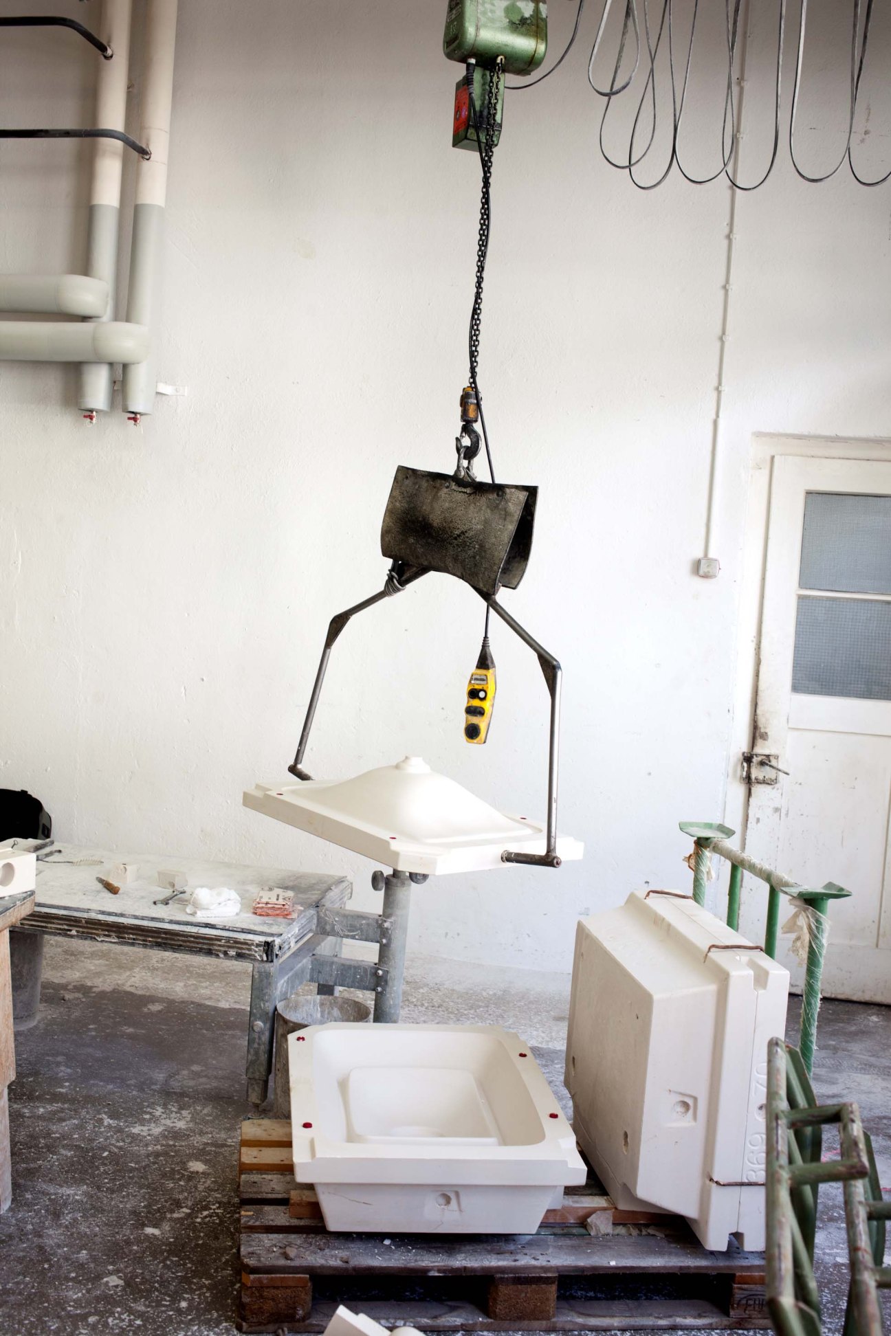 White ceramic bathroom sink being lifted by industrial pulley system in factory workshop