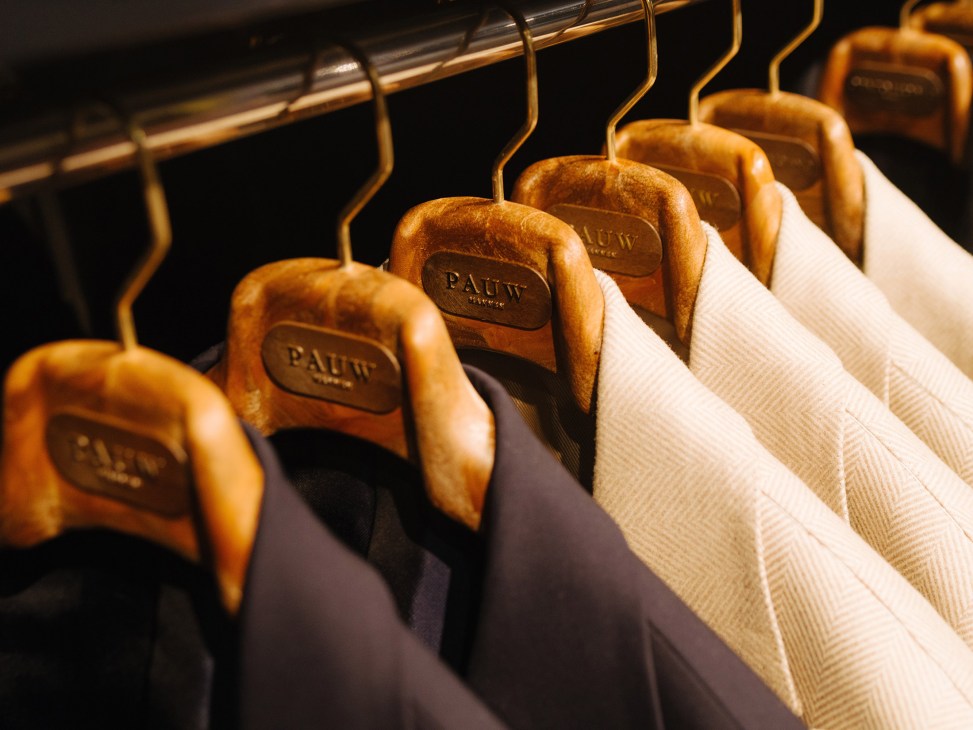 Wooden hangers branded with Pauw logo displaying tailored blazers in neutral tones at Pauw Mannen menswear store.