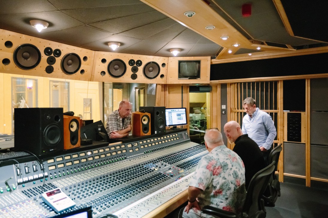 Recording studio control room with mixing console, loudspeakers, and audio engineers at work stations.