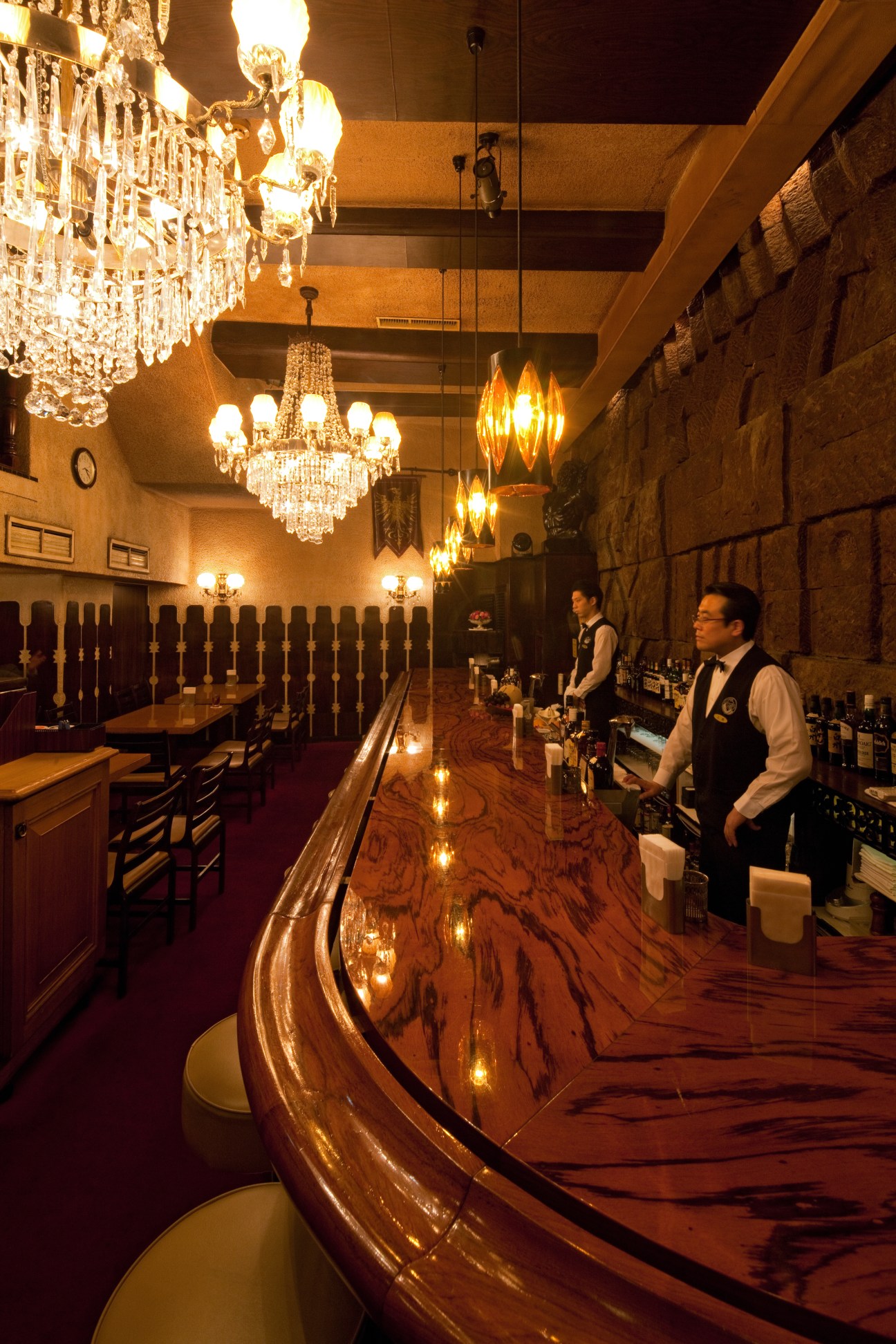 Suntory Lounge Eagle interior with curved wooden bar, crystal chandeliers, and two bartenders in bow ties