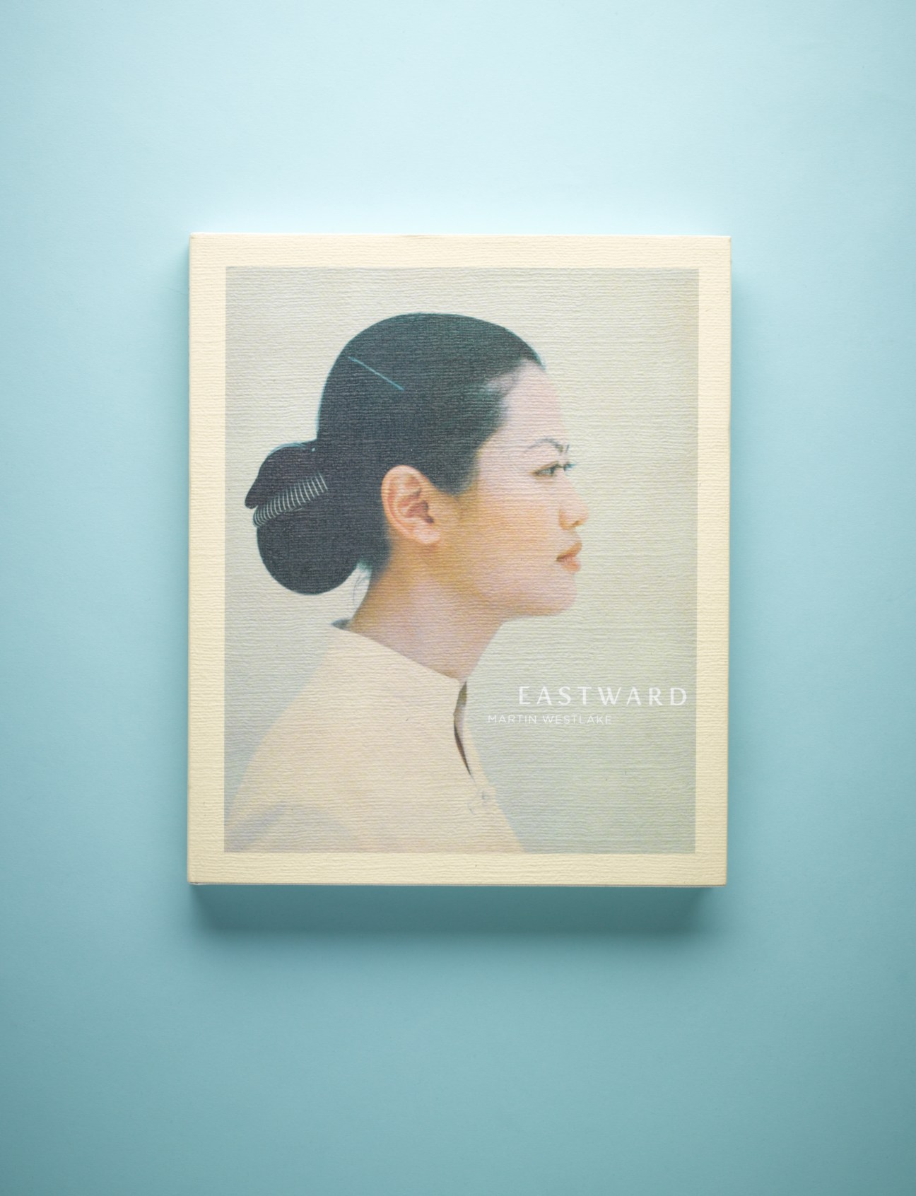 Cover of Eastward by Martin Westlake featuring a portrait of an Asian woman in profile with dark hair in a bun against a pale background.
