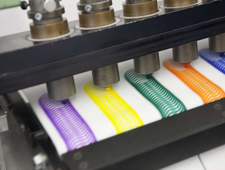 Industrial testing machine applying colored marker lines on white paper to test Edding marker longevity.