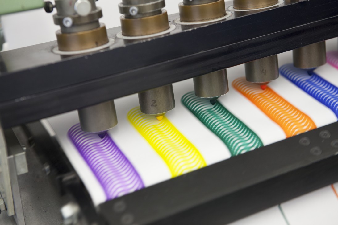 Industrial testing machine applying colored marker lines on white paper to test Edding marker longevity.