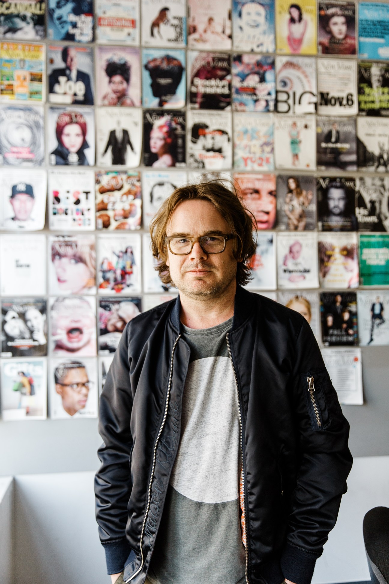 Ben Williams, digital editorial director at New York magazine, stands in front of a wall covered with magazine covers.
