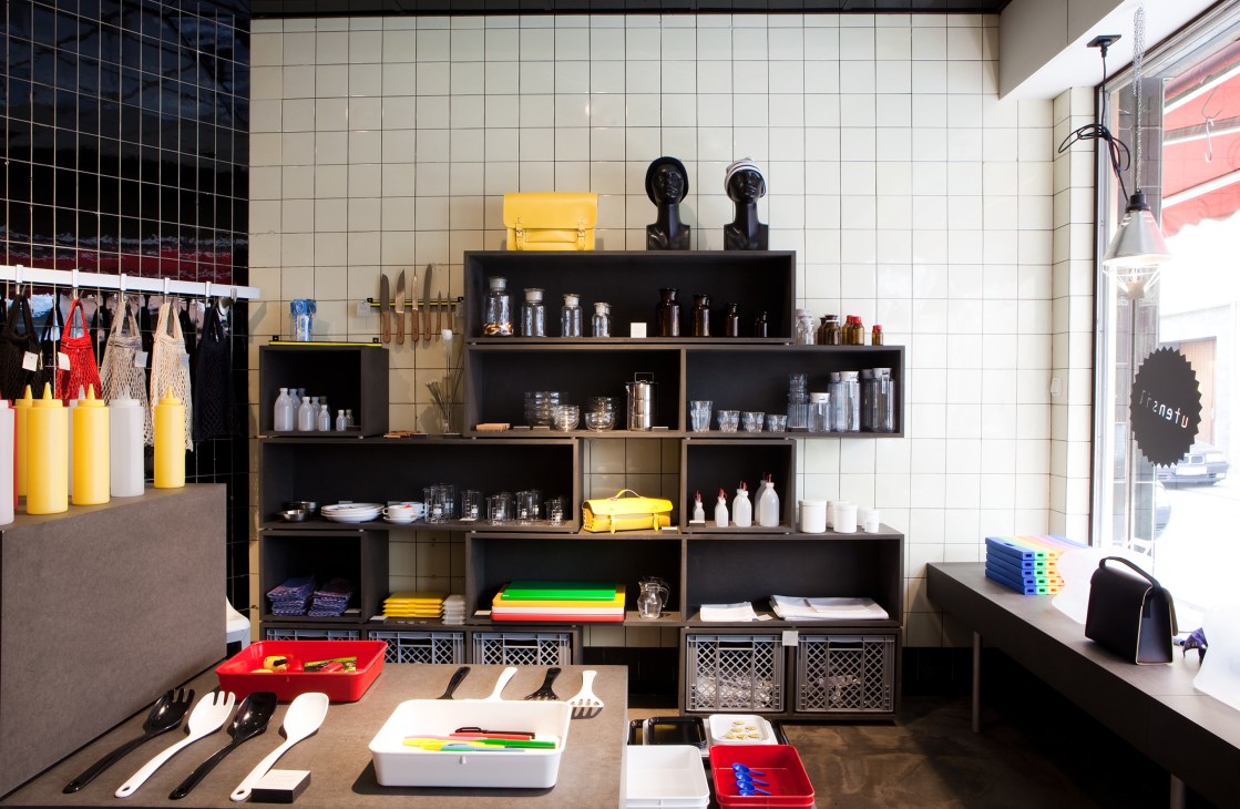 Interior of Utensil shop displaying homeware, kitchenware, and design objects on black shelving units against white tiled walls.