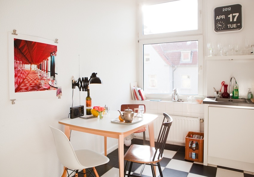 A bright, minimalist kitchen with mid-century modern furniture, red artwork on the wall, and a small dining table.