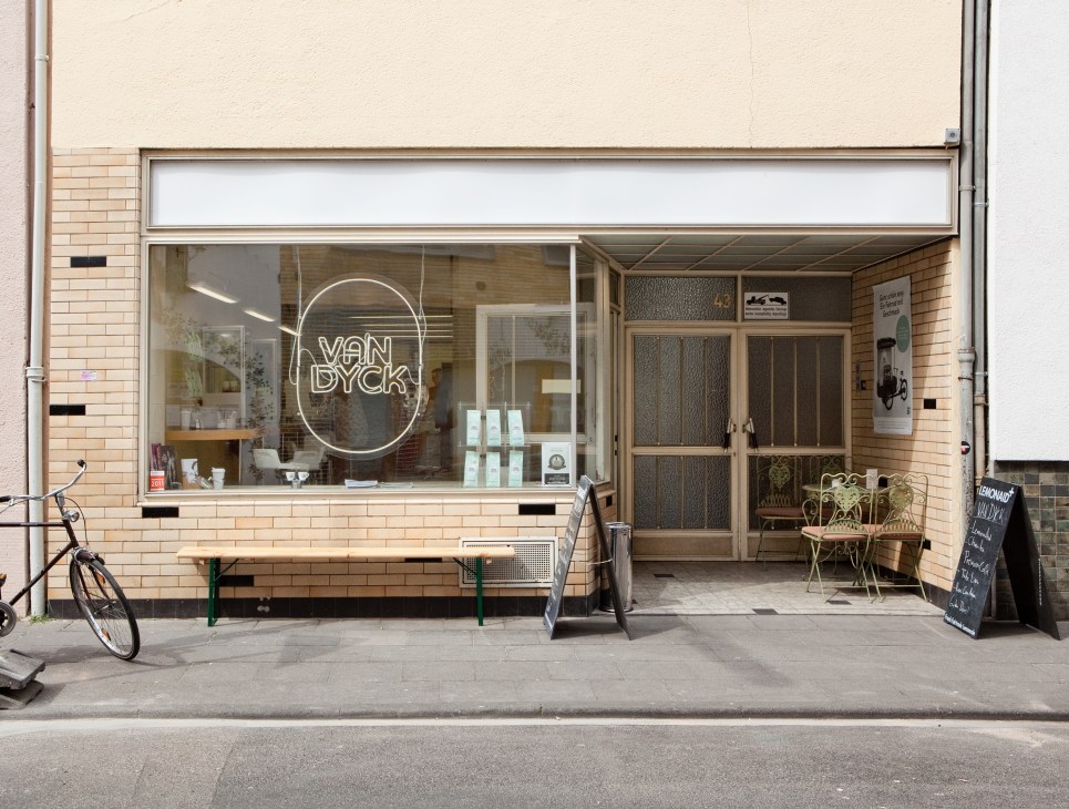 Van Dyck café storefront with neon sign, brick facade, and outdoor seating on a Köln street.