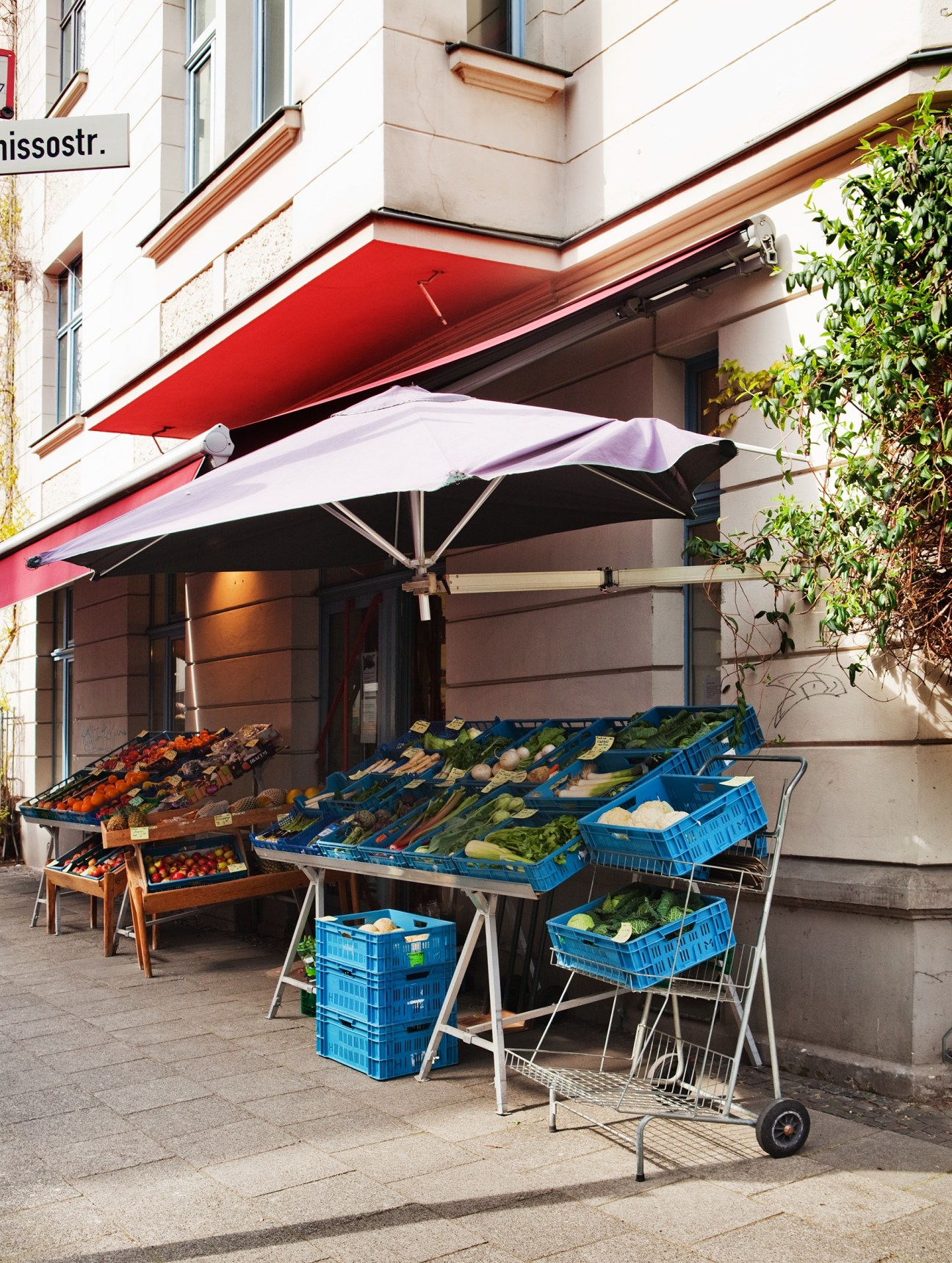 Gharavi's grocery shop storefront with red awning and blue crates of fresh produce displayed outside.