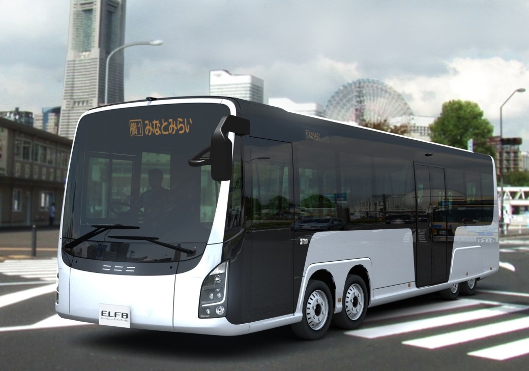 White and black eight-wheeled electric bus prototype on an urban street with modern buildings in the background.