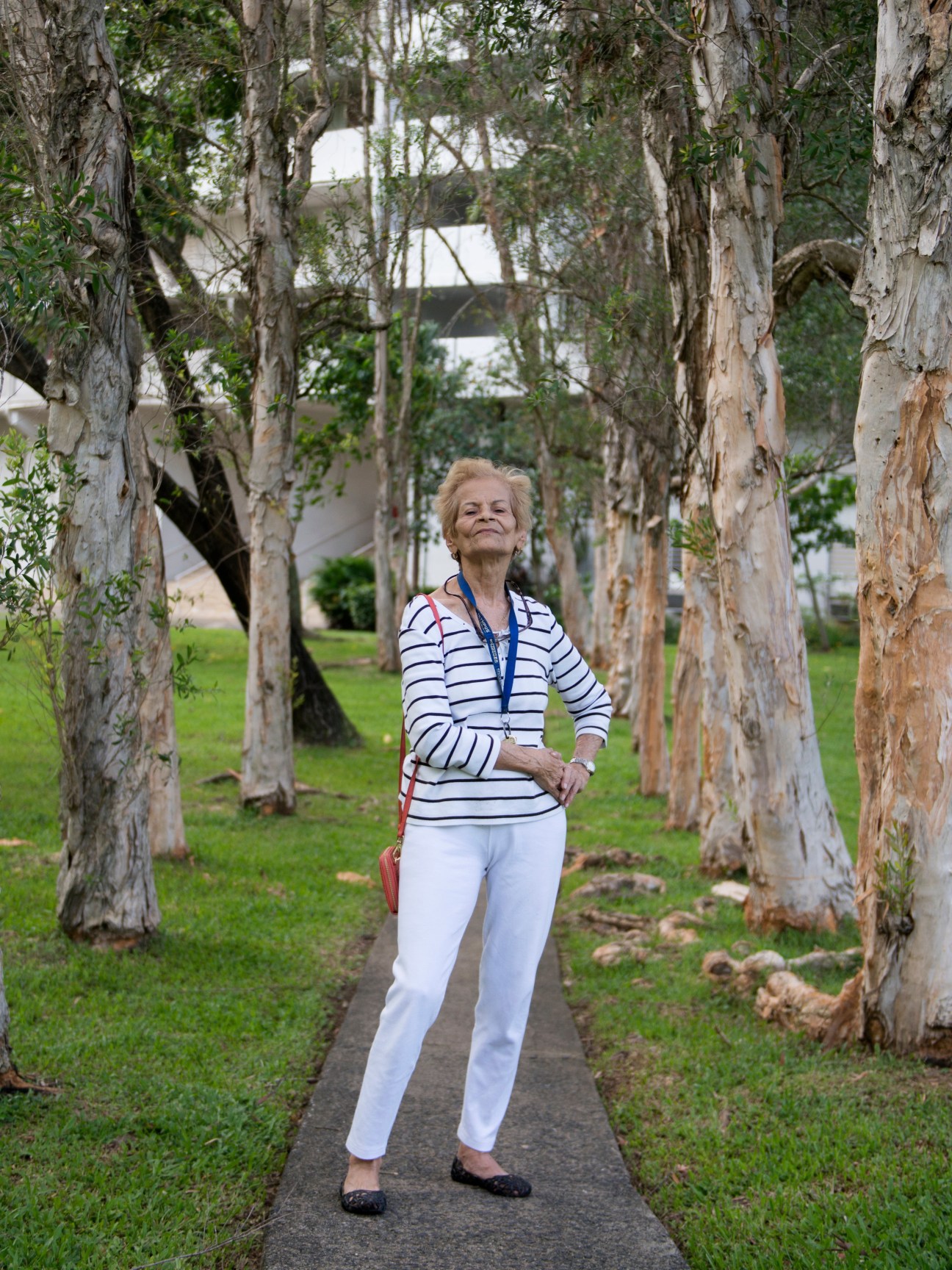 Older woman standing on a pathway lined with tall trees in El Monte's landscaped gardens.