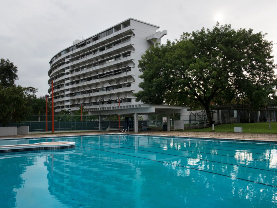 El Monte's curved modernist tower with swimming pool in foreground and tropical vegetation surrounding the complex.